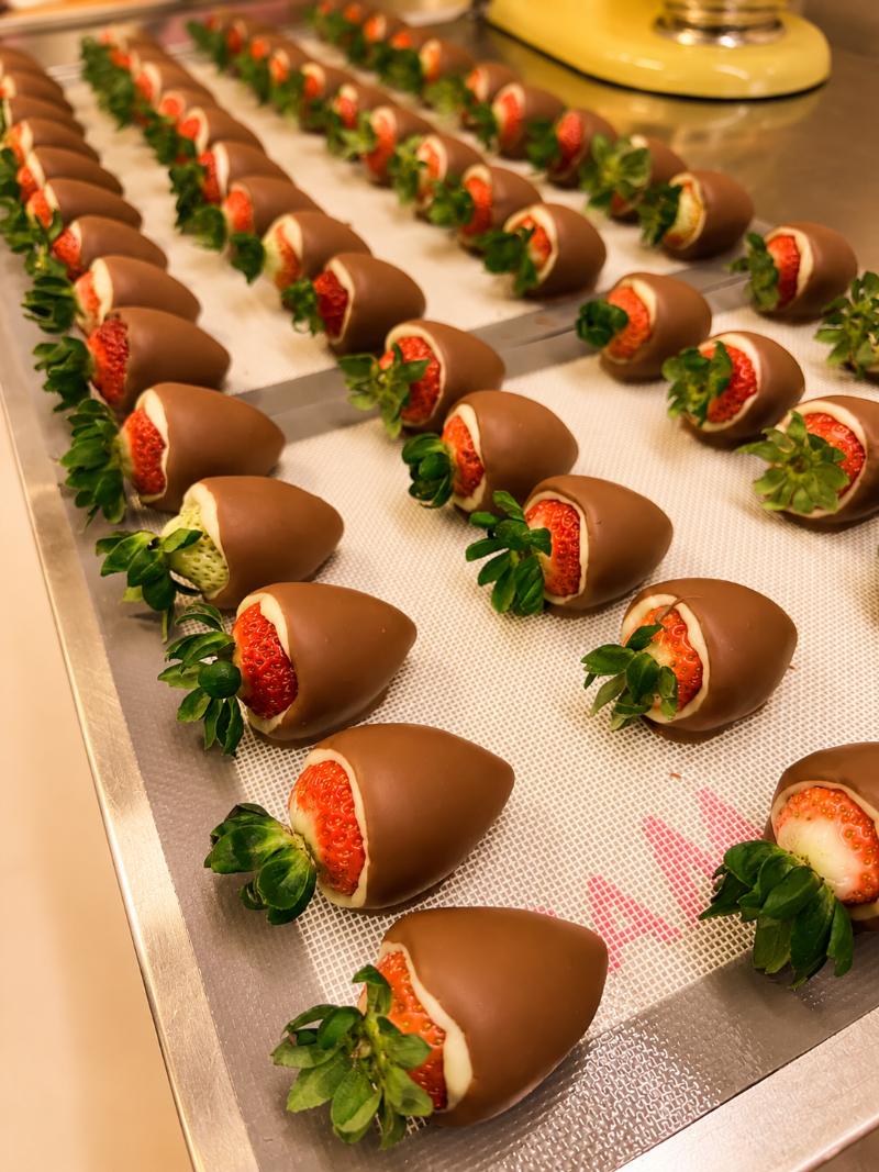 bandeja com bombons de morango finalizados, banhados em chocolate belga, com a área perto da folhinha exposta