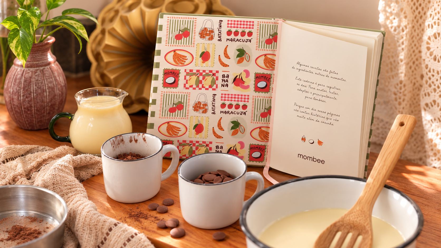 Caderno de receitas Mombee aberto ao lado de canecas com chocolate e ingredientes