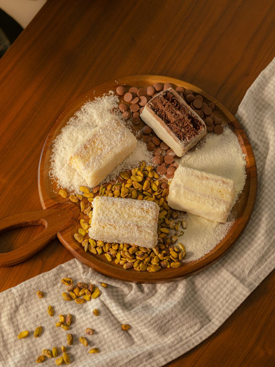 Variedade de bolos gelados em fatias sobre tábua de madeira com pistache e coco