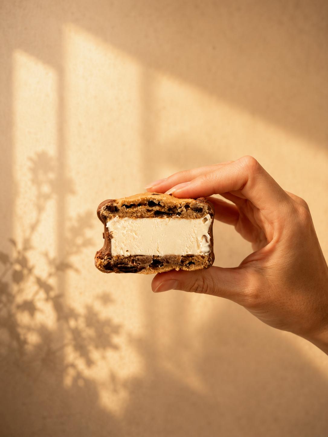 Mão segurando um ice cookie mordido, com recheio cremoso